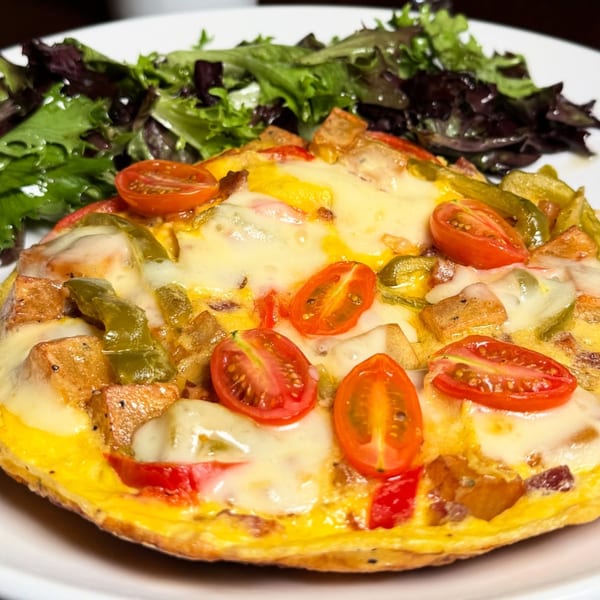 A frittata with melted cheese, cherry tomatoes, bell peppers, and potatoes, served with a side salad.