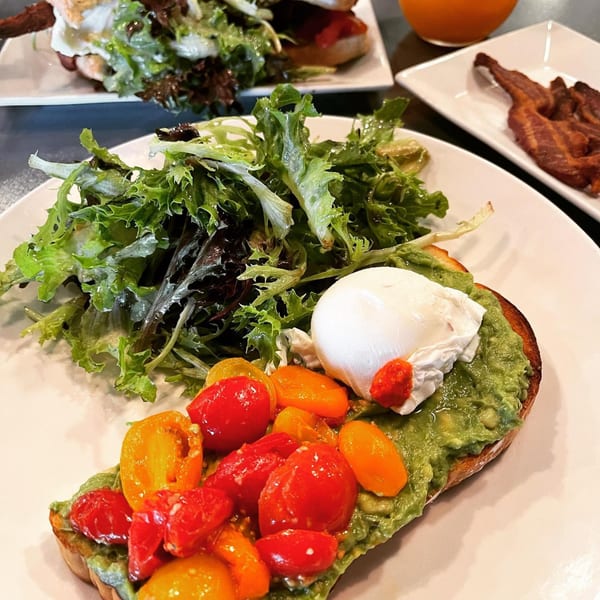 Avocado toast with poached egg, cherry tomatoes, and a side salad on a white plate.