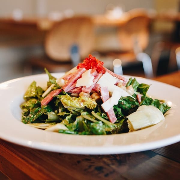 MOROSO Italian Ristorante's salad with greens, salami, cheese, and red garnish on a white plate.