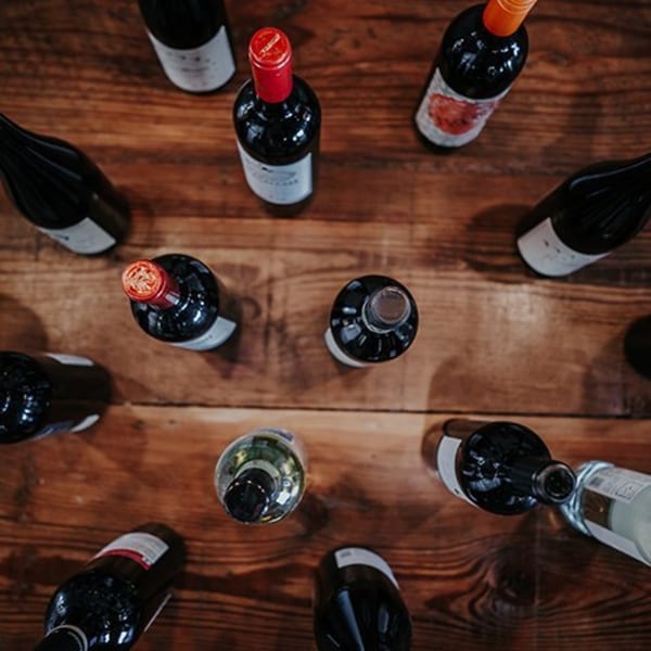 An overhead view of various red and white wine bottles scattered across a rustic wooden table.
