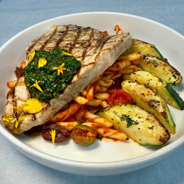 Grilled swordfish topped with pesto and yellow edible flowers, served with pasta and zucchini.