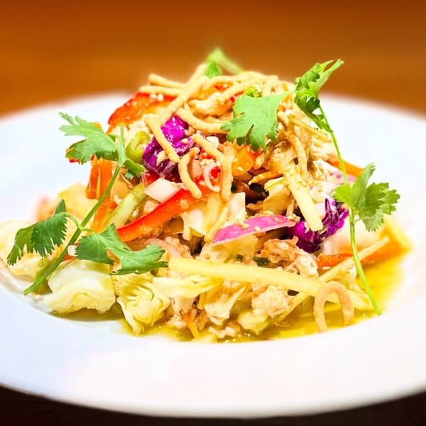 Colorful salad with red cabbage, bell peppers, cilantro, and crispy noodles on a white plate.