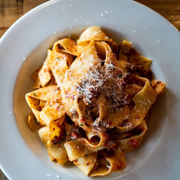 Close-up of pappardelle pasta with bolognese sauce and grated Parmesan cheese in a white bowl.