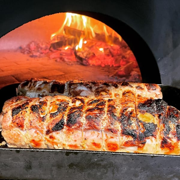 Two large cuts of meat roasting in a wood-fired oven with visible flames.