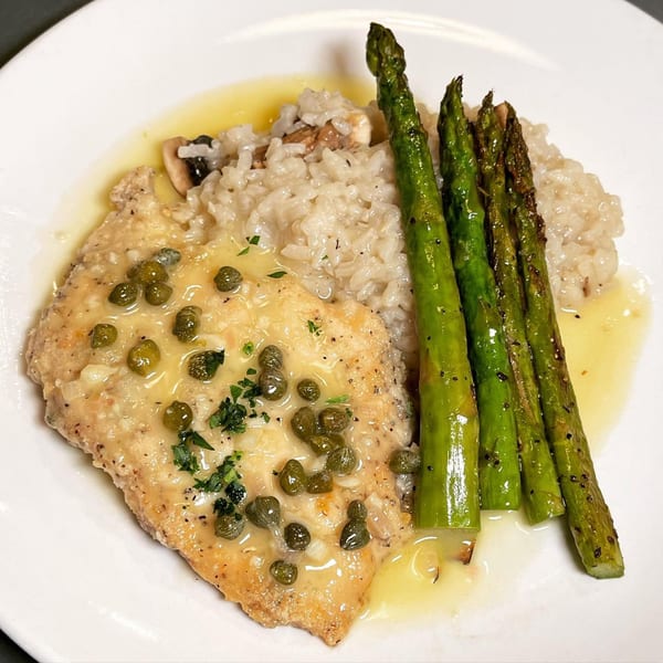 Chicken piccata with capers, lemon sauce, mushroom risotto, and grilled asparagus on a white plate.