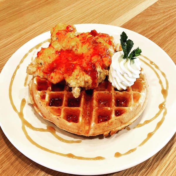 Crispy fried chicken with red sauce on a waffle, topped with whipped cream and mint.