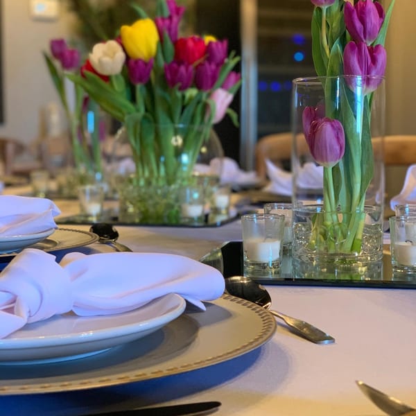 A set table with white plates, napkins, silverware, and colorful tulip centerpieces.