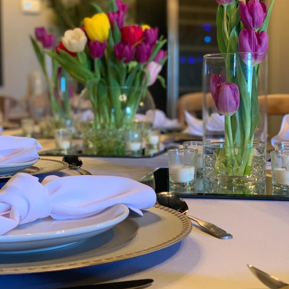 A set table with white plates, napkins, silverware, and colorful tulip centerpieces.