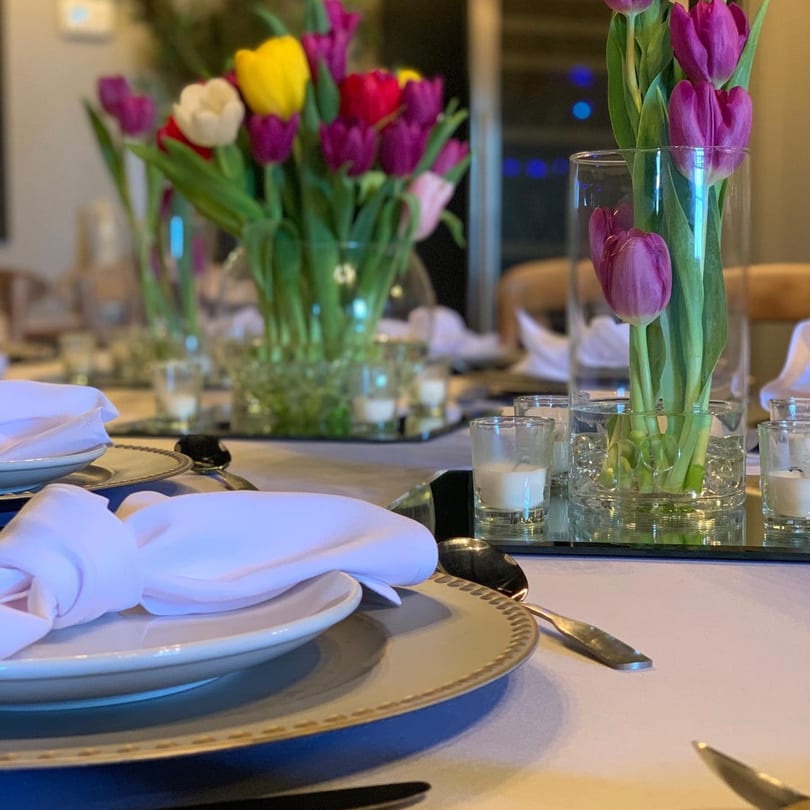 A set table with white plates, napkins, silverware, and colorful tulip centerpieces.