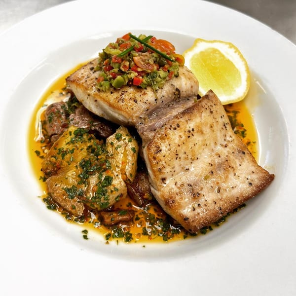 MOROSO's Italian fish dish with salsa, roasted potatoes, and a lemon wedge on a white plate.