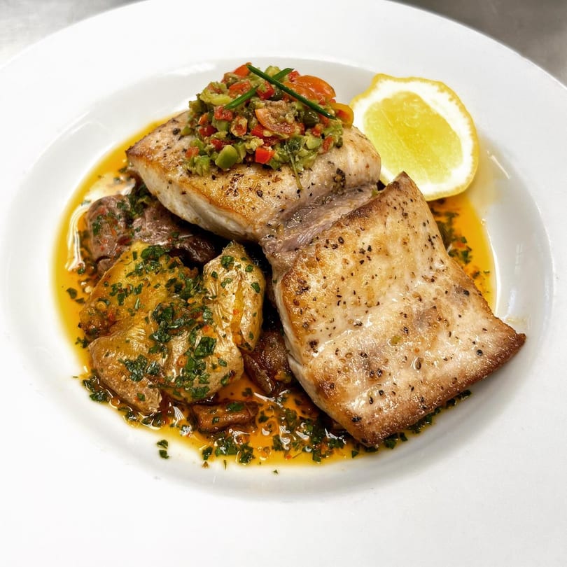 MOROSO's Italian fish dish with salsa, roasted potatoes, and a lemon wedge on a white plate.
