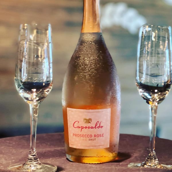 Chilled bottle of Caposaldo Prosecco Rosé and two empty champagne flutes on a table.