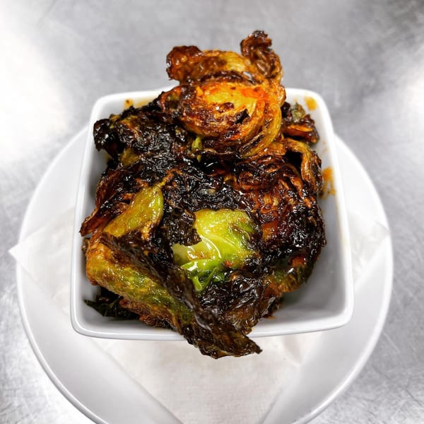 Crispy, dark-roasted Brussels sprouts with a glossy glaze, served in a white square bowl on a white plate.